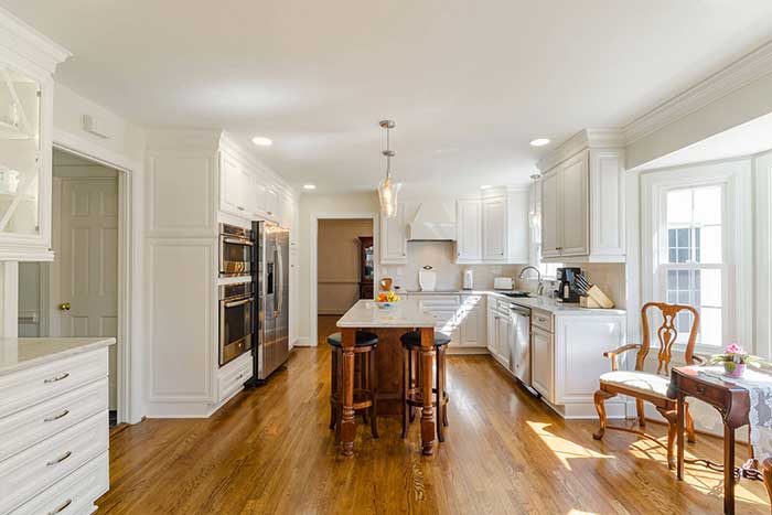 A galley kitchen with white cabients and walls and honey colored wood floors